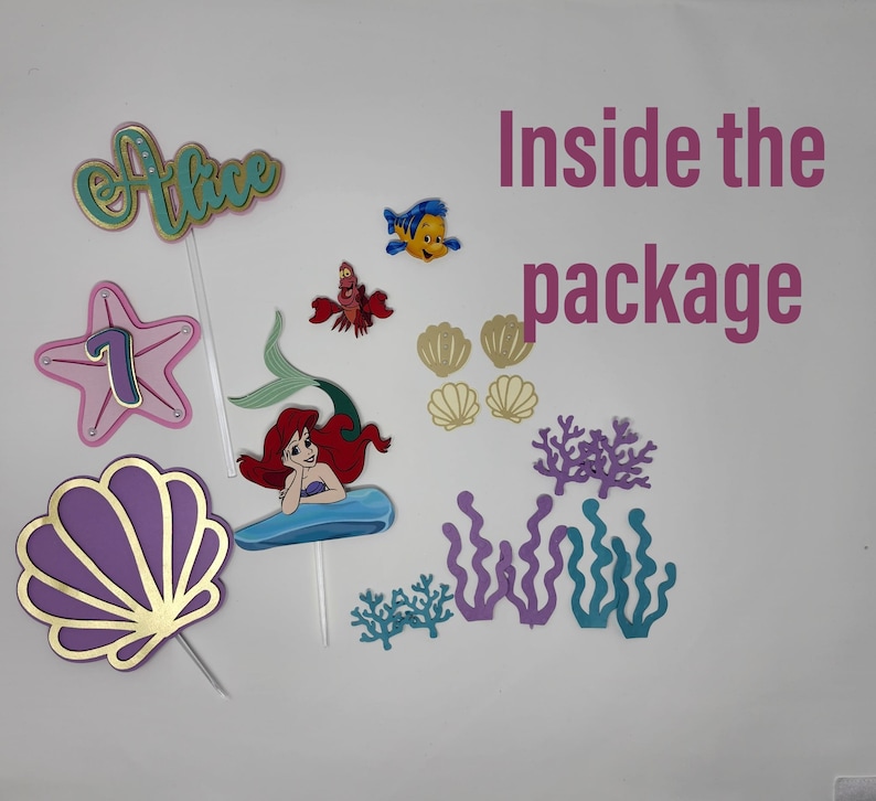 May include: A set of mermaid-themed cake toppers, including a purple seashell, a starfish with the number 7, a mermaid with red hair, a blue fish, a red crab, and various seaweeds. The text "Alice" and "Inside the package" are also included.
