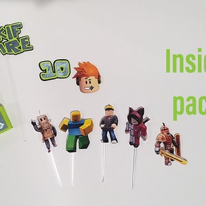 May include: A set of Roblox themed cake toppers, including a Roblox logo, a number 10, a Roblox character, and several other Roblox characters. The cake toppers are on white sticks and are ready to be placed on a cake.