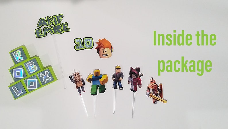 May include: A set of Roblox themed cake toppers, including a Roblox logo, a number 10, a Roblox character, and several other Roblox characters. The cake toppers are on white sticks and are ready to be placed on a cake.