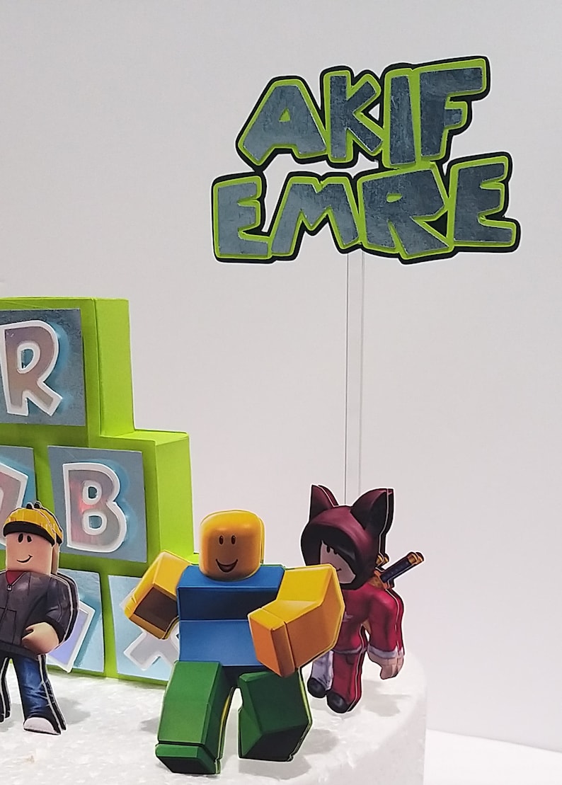 May include: A birthday cake decorated with a Roblox theme. The cake is decorated with green and blue blocks, a Roblox character, and a topper that says "AKIF EMRE".