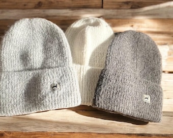 Può includere: Tre berretti invernali di lana in diversi colori: grigio chiaro, bianco e grigio scuro. Ogni berretto ha una piccola toppa con il logo sul lato.