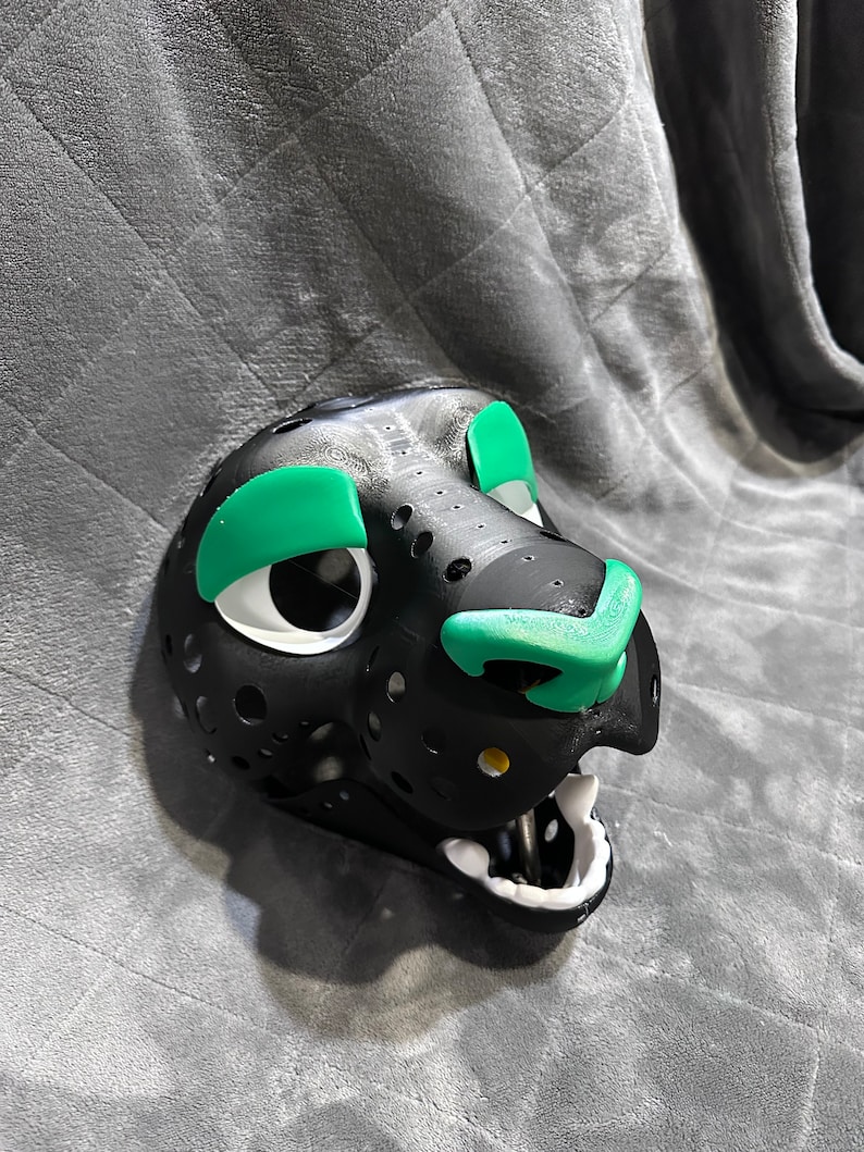 Puede incluir: M&aacute;scara de animal de piel negra y blanca con detalles verdes alrededor de los ojos y la nariz. La m&aacute;scara tiene un dise&ntilde;o detallado con agujeros en toda la superficie.