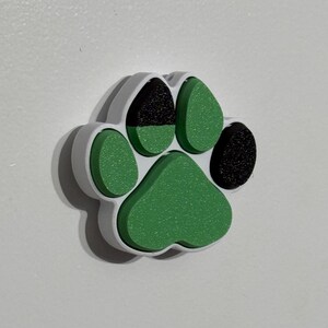 May include: A white, green, and black paw print charm. The charm is made of plastic and has a 3D design.