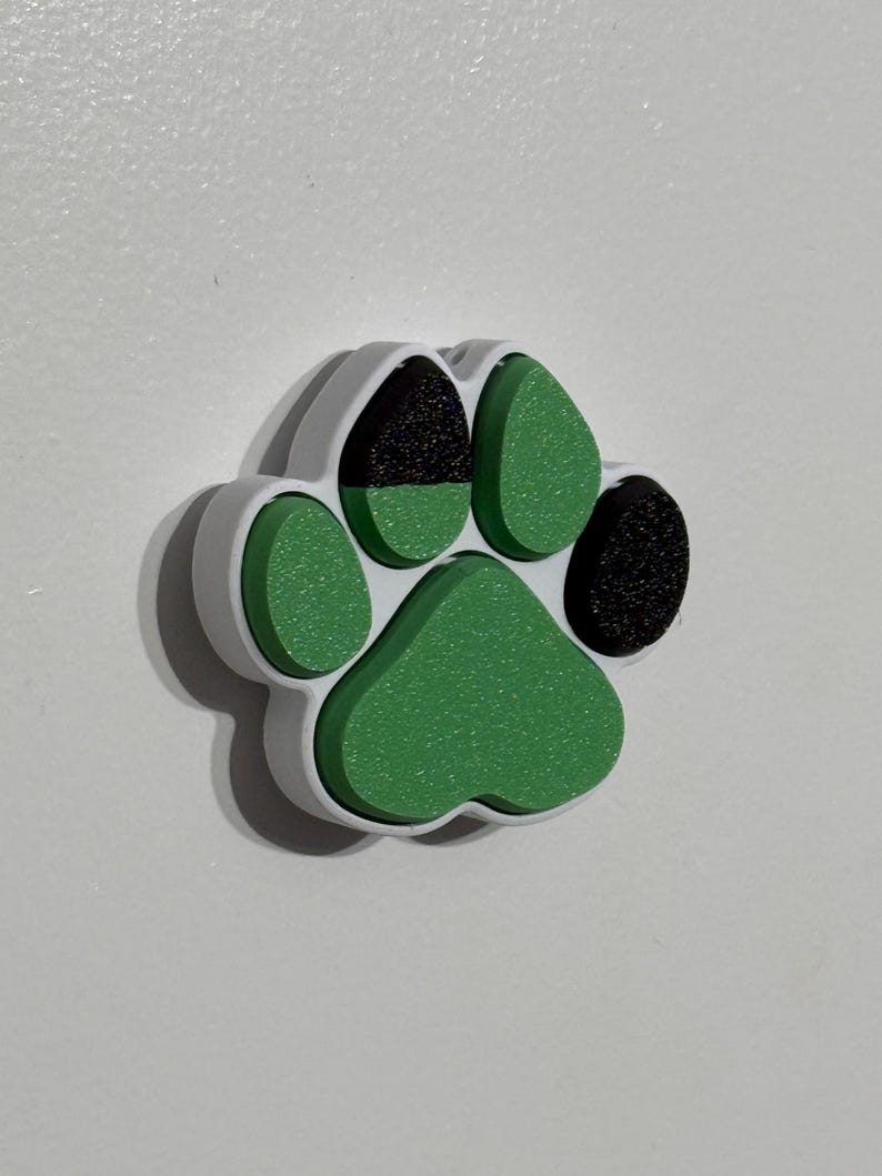 May include: A white, green, and black paw print charm. The charm is made of plastic and has a 3D design.