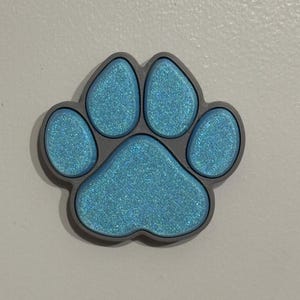 May include: A blue glitter paw print charm with a gray outline.