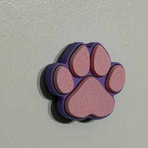 May include: A purple paw print with pink raised details. The paw print is made of a soft, textured material.