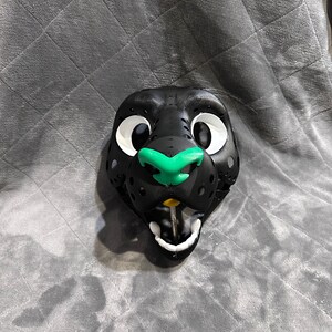 Puede incluir: Cabeza de fursuit negra y verde con grandes ojos blancos y una sonrisa de dientes. La cabeza est&aacute; hecha de espuma y tiene un aspecto realista.
