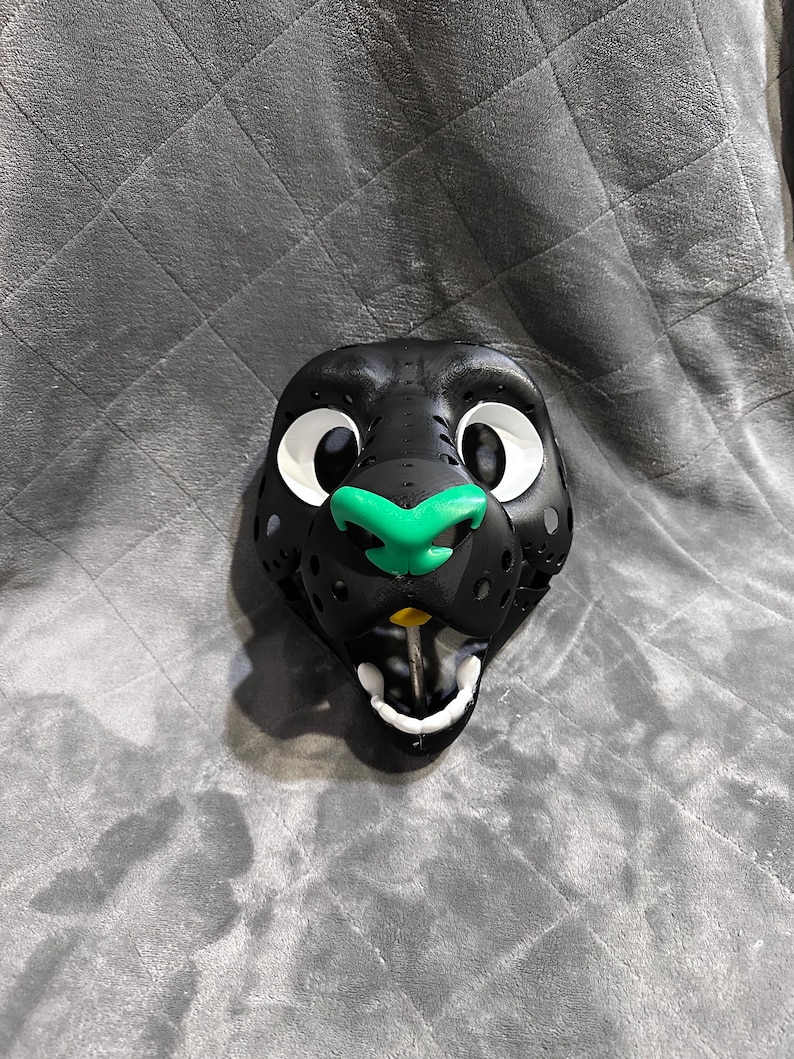 Puede incluir: Cabeza de fursuit negra y verde con grandes ojos blancos y una sonrisa de dientes. La cabeza est&aacute; hecha de espuma y tiene un aspecto realista.