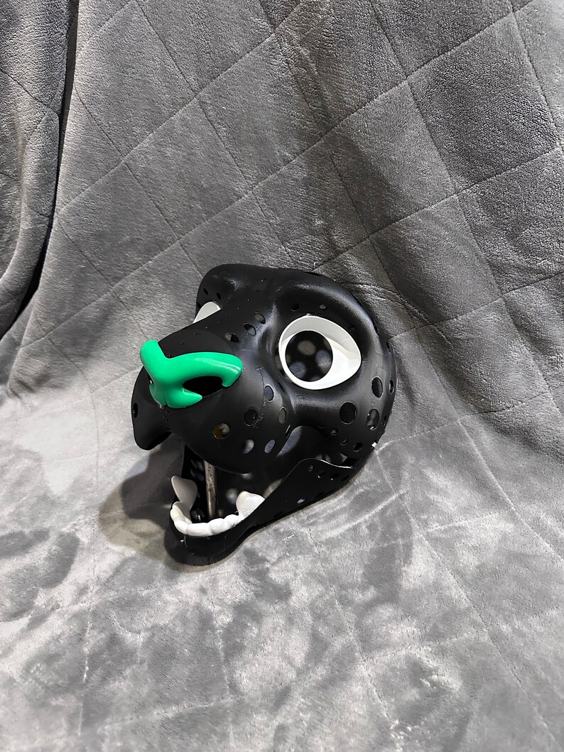 Puede incluir: M&aacute;scara de animal de peluche negro y blanco con nariz verde y ojos blancos. La m&aacute;scara est&aacute; hecha de un material ligero y tiene un dise&ntilde;o detallado.