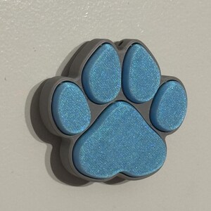 May include: A blue paw print with glitter, made of plastic, with a gray outline.