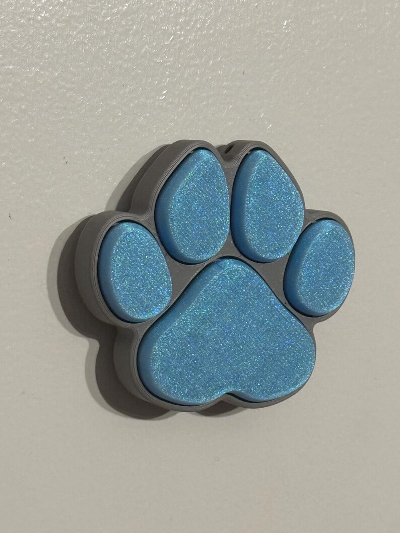 May include: A blue paw print with glitter, made of plastic, with a gray outline.