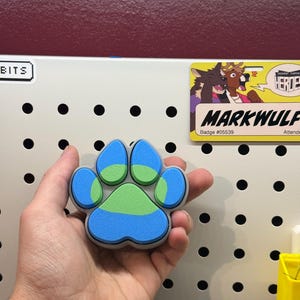 May include: A blue, green, and gray paw print charm. The paw print is made of a soft, squishy material.