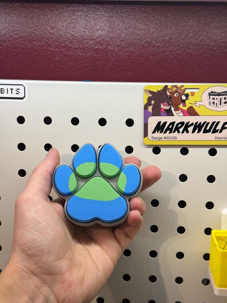 May include: A blue, green, and gray paw print charm. The paw print is made of a soft, squishy material.