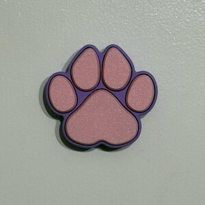 May include: A purple paw print with pink accents. The paw print is made of a textured material.