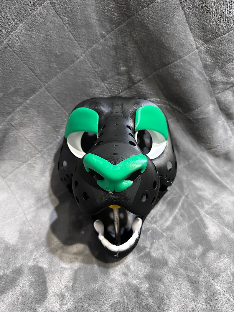 Puede incluir: M&aacute;scara de animal de peluche negra y verde con boca y nariz blancas. La m&aacute;scara tiene un aspecto realista y est&aacute; hecha de un material suave y afelpado.