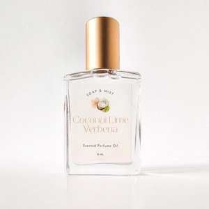 May include: A clear glass perfume oil bottle with a gold cap. The label reads "Soap & Mist Coconut Lime Verbena Scented Perfume Oil 15 ml". The bottle is rectangular with rounded edges and sits on a white surface.