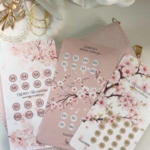 以下が含まれることがあります： 桜のイラストとドル金額が記載された円形のトラッキングスポットが特徴の、3枚の長方形の貯金チャレンジカード。カードには「Cherry Blossom savings challenge」、「Sakura savings challenge」、「Pink Cherry Blossom savings challenge」と記載されています。