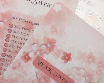 May include: Pink floral-patterned savings tracker with the text "MY $3K SAVINGS." The tracker includes sections to complete and a sticker with the same text. The design features pink cherry blossoms.