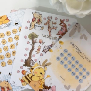 May include: Three rectangular paper savings challenge trackers featuring Winnie the Pooh and friends. The cards display colourful illustrations of characters, pink circular icons for tracking, and text including "Baby Winnie & Friends" and "Fun Day with Friends" with dollar amounts.