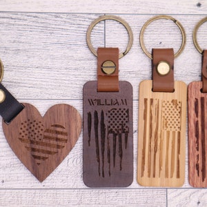May include: Four wooden keychains with leather straps and metal rings. One keychain is heart-shaped with an American flag design. The other three keychains are rectangular with American flag designs. One of the rectangular keychains has the name "William" engraved on it.