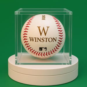 May include: A white baseball with red stitching and the name "W Winston" in gold lettering. The baseball is in a clear display case on a white pedestal.