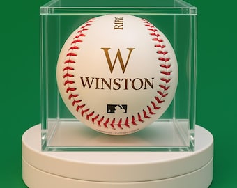May include: A white baseball with red stitching encased in a clear acrylic display cube. The ball features the gold letter W, the name WINSTON, the text RIRC, and the official MLB logo printed on the surface, which also reads AUTHENTIC LEATHER COVER.