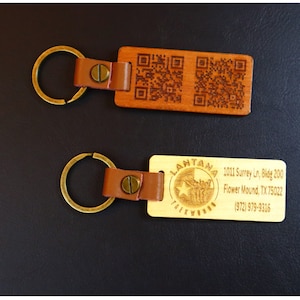 May include: Two wooden keychains with leather straps. The first keychain has two QR codes and the second keychain has the text "LANTANA TAEKWONDO" and contact information for a business.