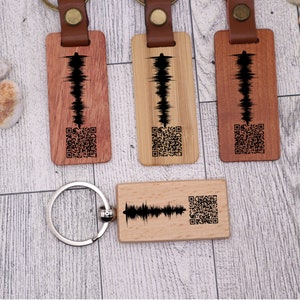 May include: Three wooden keychains with a sound wave design and a QR code. The keychains are brown, light brown, and natural wood. The keychains are attached to silver key rings.