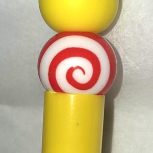 May include: A novelty pen featuring a cartoon figure with yellow hair and a blue suit. The pen has a yellow barrel, a red and white swirled ball, and a yellow top. The figure has a red tie.