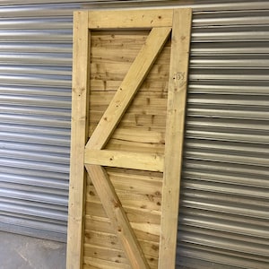 May include: A wooden gate with a diagonal brace design. The gate is made of natural wood with a light brown color.