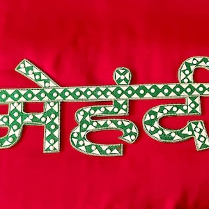 May include: Green and white decorative letters spelling out the word "Mehndi" on a red background.