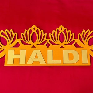 May include: A yellow sign with the word "HALDI" in gold letters. The sign is decorated with four lotus flower cutouts.