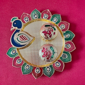 May include: A gold-colored metal tray with a peacock design. The tray has a blue peacock with green and red accents. The tray is decorated with a grid pattern and has two circular compartments with red and green floral designs.
