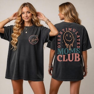 Könnte beinhalten: Dunkelgraues T-Shirt mit dem Text "Mom's Club" auf der Vorderseite und "Overstimulated Moms Club" auf der Rückseite. Das Design auf der Vorderseite ist ein rosa Kreis mit den Worten "Mom's" und einem Smiley. Das Design auf der Rückseite hat einen schmelzenden Smiley.
