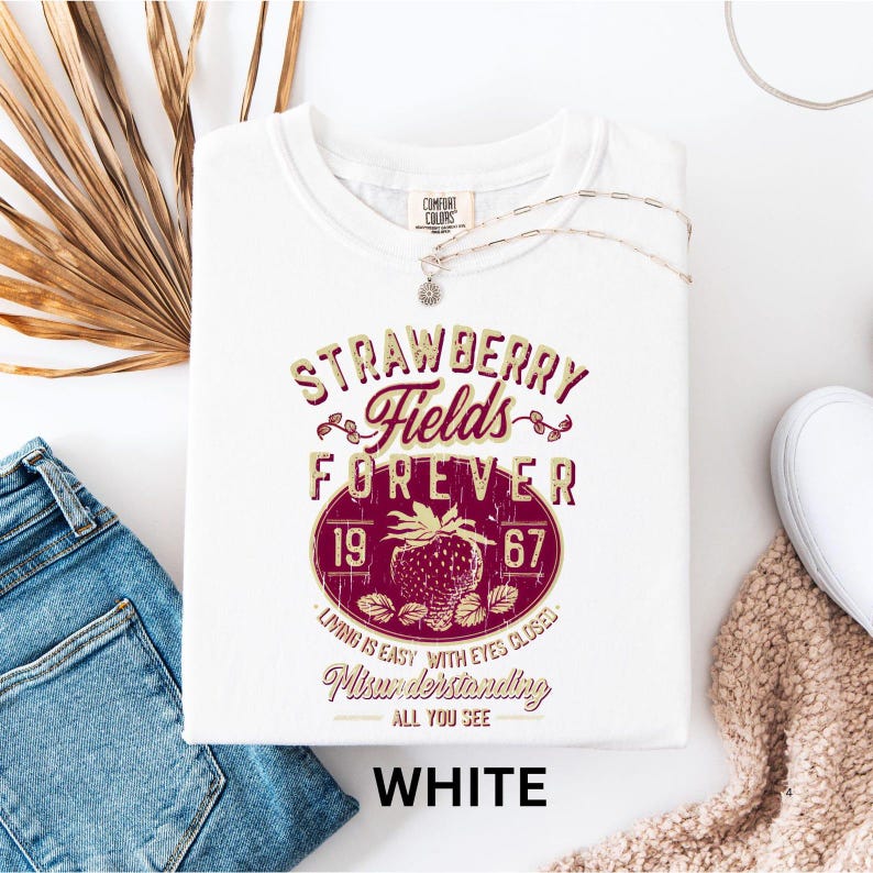 a white t-shirt with a graphic design, a pair of blue jeans, and some accessories such as a necklace and a scarf, all laid out on a white background.