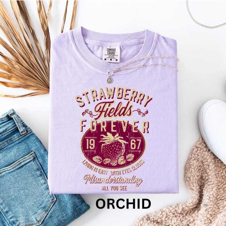 a purple t-shirt with a graphic design, a pair of blue jeans, a white sneaker, and some dried leaves, all arranged on a white background.