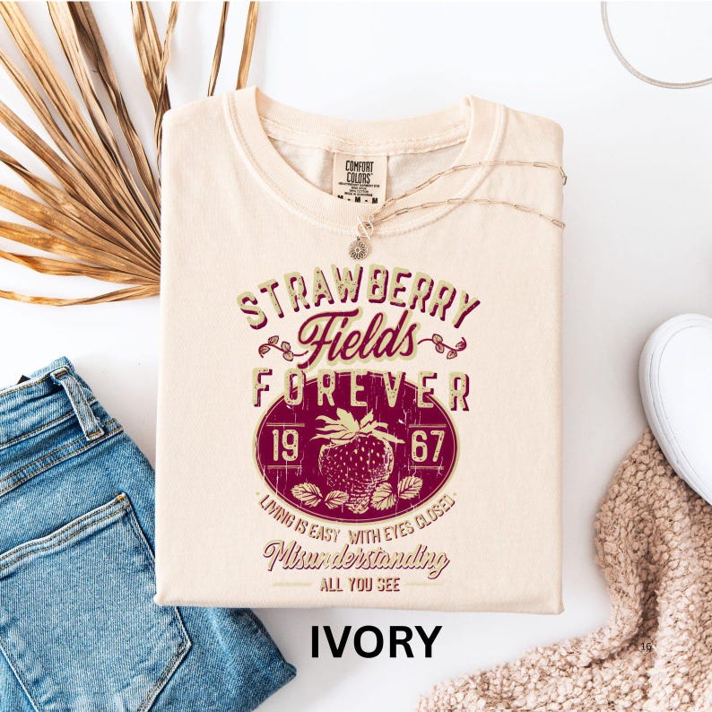 a white t-shirt with a vintage-style design, a pair of blue jeans, and some beige and brown textured fabric, all laid out on a white background.