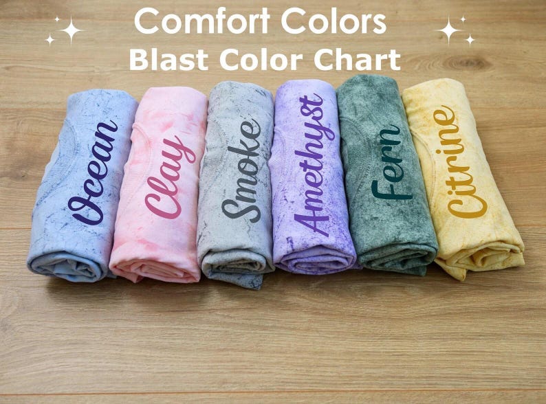 A collection of six rolled-up towels or cloths, each with a different color printed on them, arranged on a wooden surface.