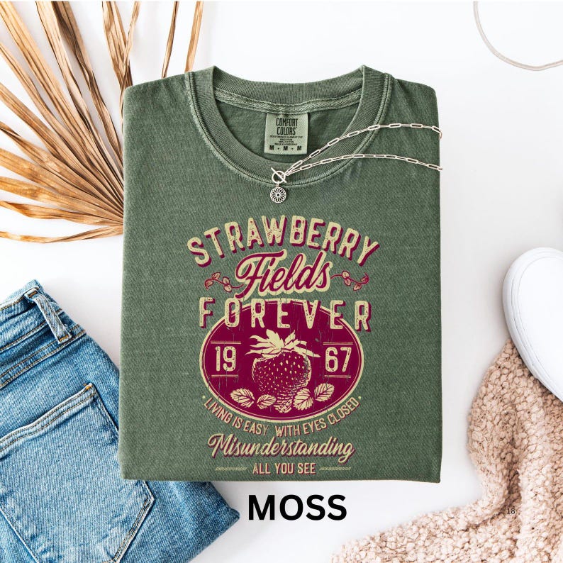 a green t-shirt with a graphic design, a pair of blue jeans, and some other clothing items, all laid out on a white background.