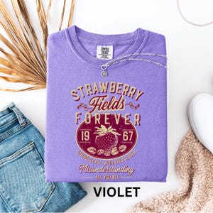 a purple t-shirt with a graphic design, a pair of blue jeans, and some other clothing items, all laid out on a white background.