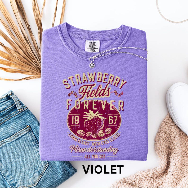 a purple t-shirt with a graphic design, a pair of blue jeans, and some other clothing items, all laid out on a white background.