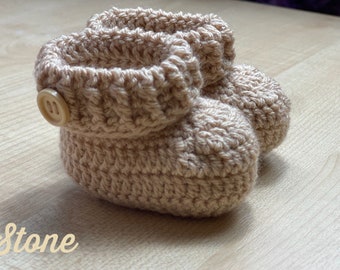 May include: A pair of beige crocheted baby booties with a button on the top of each bootie.