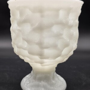 May include: A white, textured glass goblet with a footed base. The goblet has a unique, bubbly texture on the exterior, giving it a frosted appearance. The stem and base are also textured, creating a cohesive design.