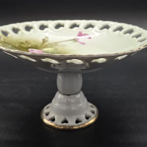 Puede incluir: Una taza de cerámica blanca con un asa negra y el texto "But First, Coffee" en negrita negra. La taza está llena de un líquido oscuro, probablemente café, y se encuentra sobre una superficie clara.