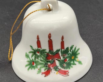 Pequeña campana navideña con velas rojas y ramas de pino.