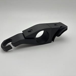 May include: A black, angular metal clamp with a circular opening and a hook-shaped end. The clamp has a hinged section and is secured with a screw. The object is set against a plain white background.