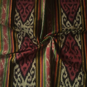 以下が含まれることがあります： 黒、白、赤、緑、黄色のストライプ模様の織物。生地は伝統的なイカットのデザインで、幾何学模様が繰り返されています。