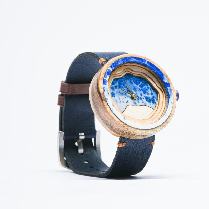 May include: A wooden wristwatch with a blue and white resin face. The watch has a dark blue leather band.