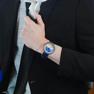 May include: A blue and white wristwatch with a gold rim and a blue leather band. The watch face has a blue and white wave design.