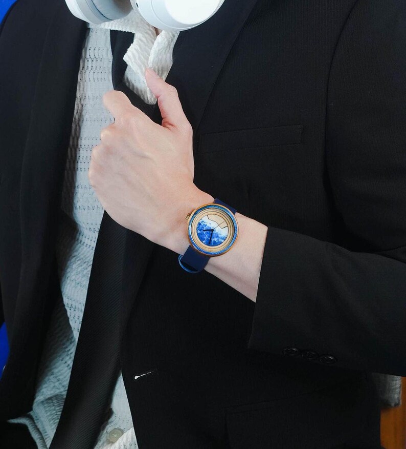 May include: A blue and white wristwatch with a gold rim and a blue leather band. The watch face has a blue and white wave design.
